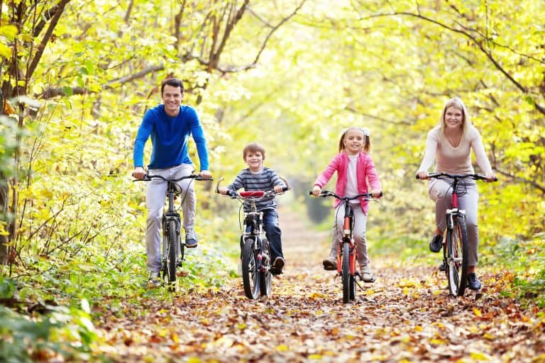 Family riding bikes on a forest trail during fall.